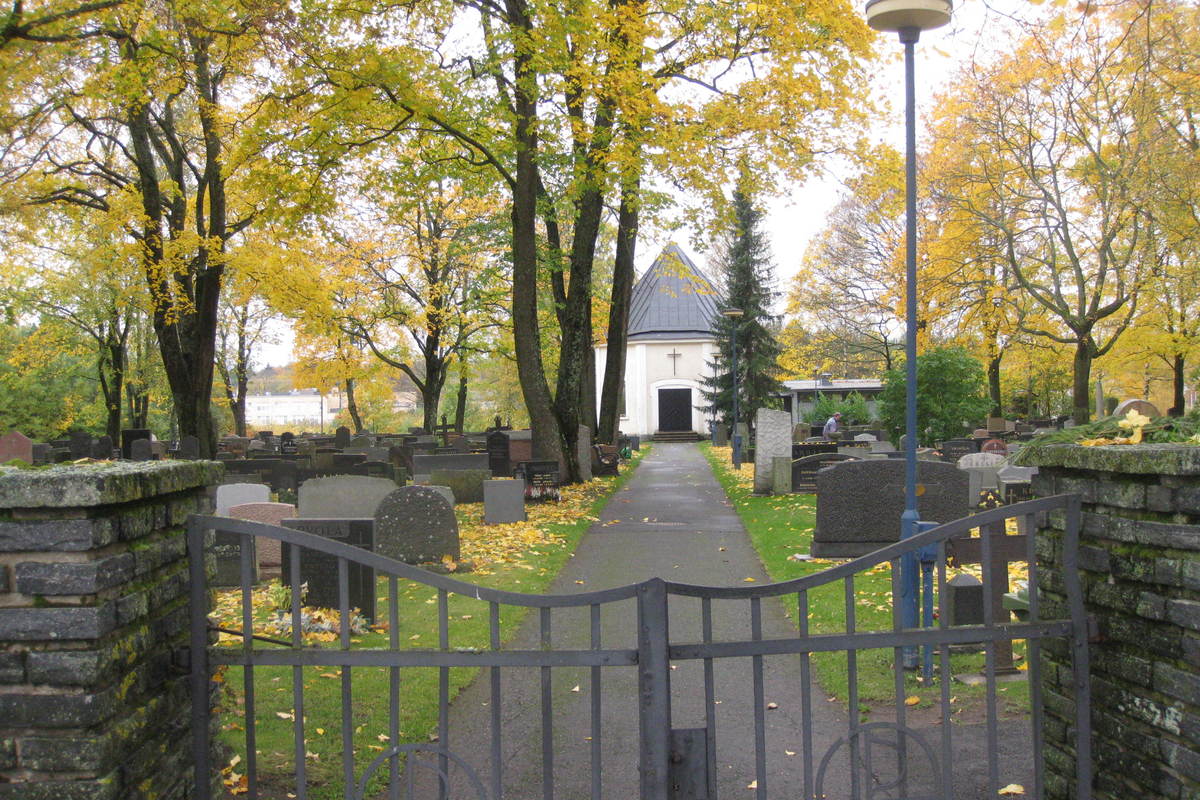 Rautaportin takana avautuva käytävä, jonka molemmin puolin on hautakiviä ja päässä valkoinen pieni kappeli.