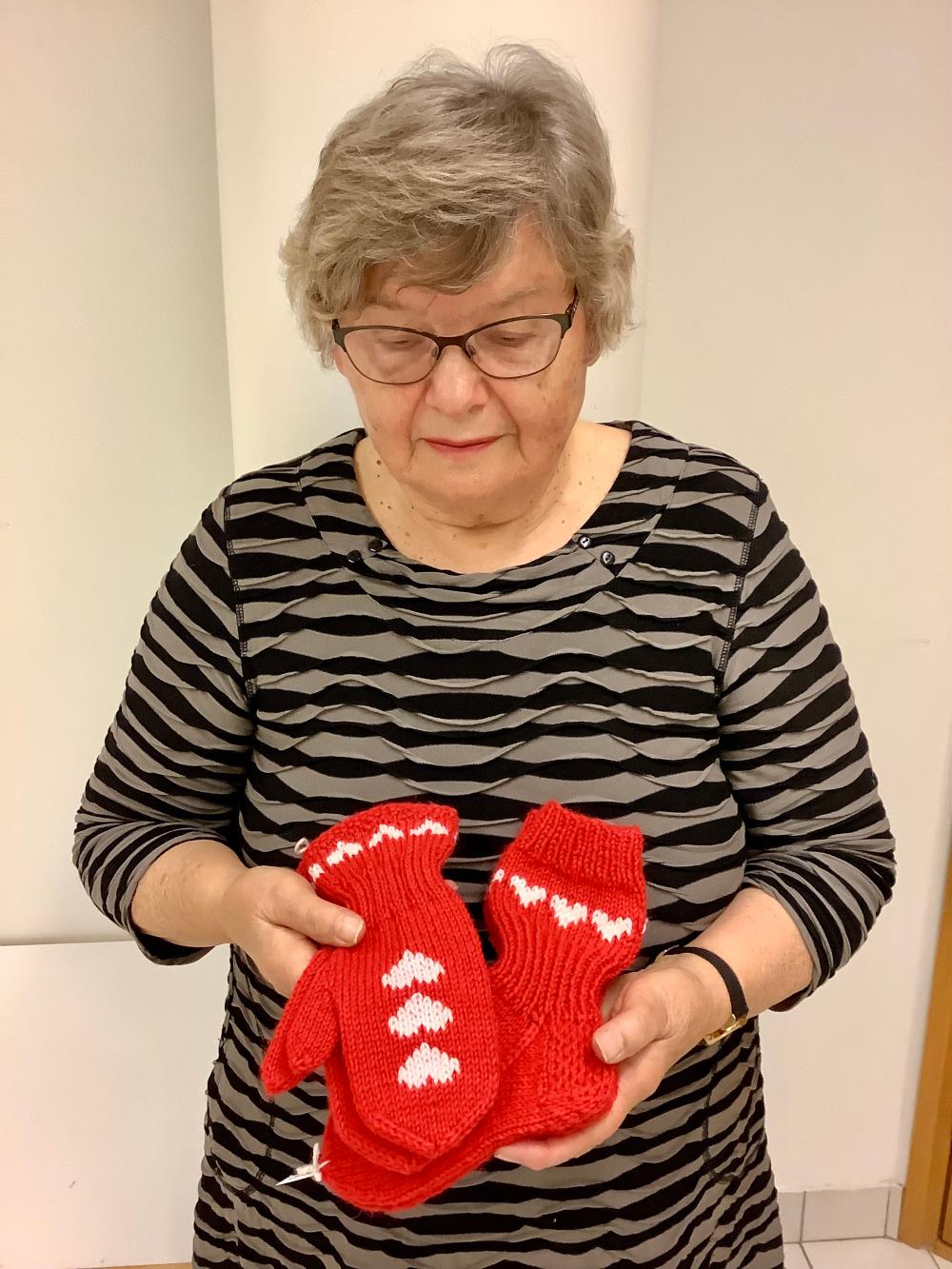 Nainen esittelee punaisia lapasi ja sukkia, joissa on valkoisia sydämiä.