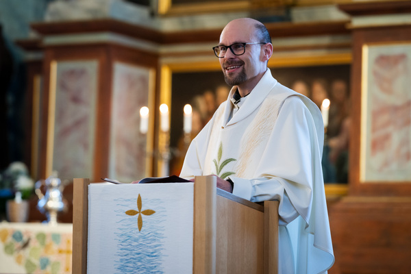 Pappi, vaalea messukasukka ja lukupulpetin liina.