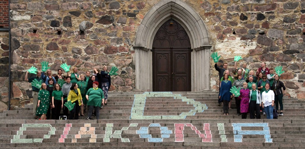 Iso D-kirjain ja diakonia-teksti väritetty liiduilla Tuomiokirkon portaille, ympärillä diakoniatyöntekijöitä.
