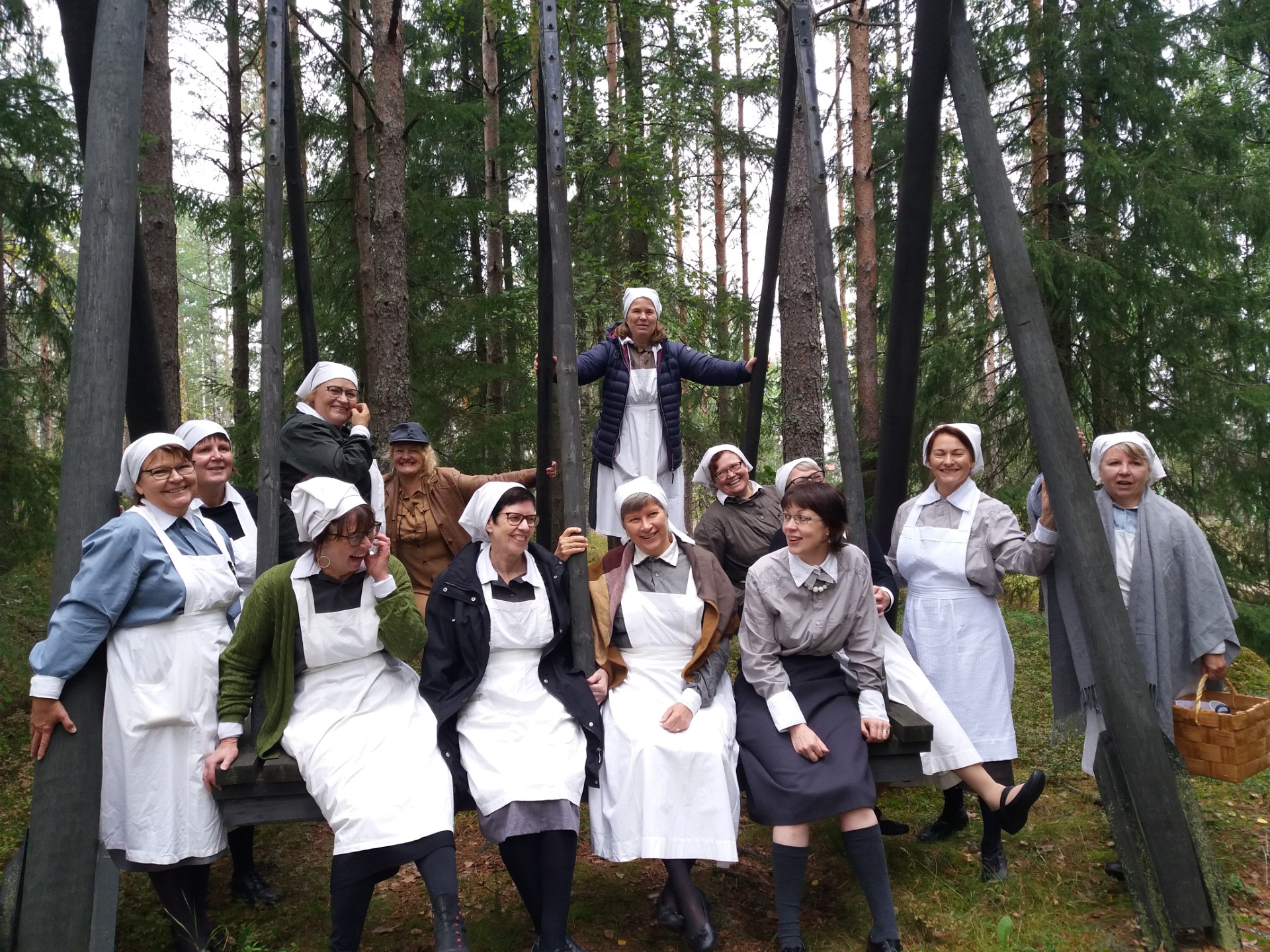 Iso rivi naisia vanhanaikaiset mekot ja essut päällä ja hilkat päässä.