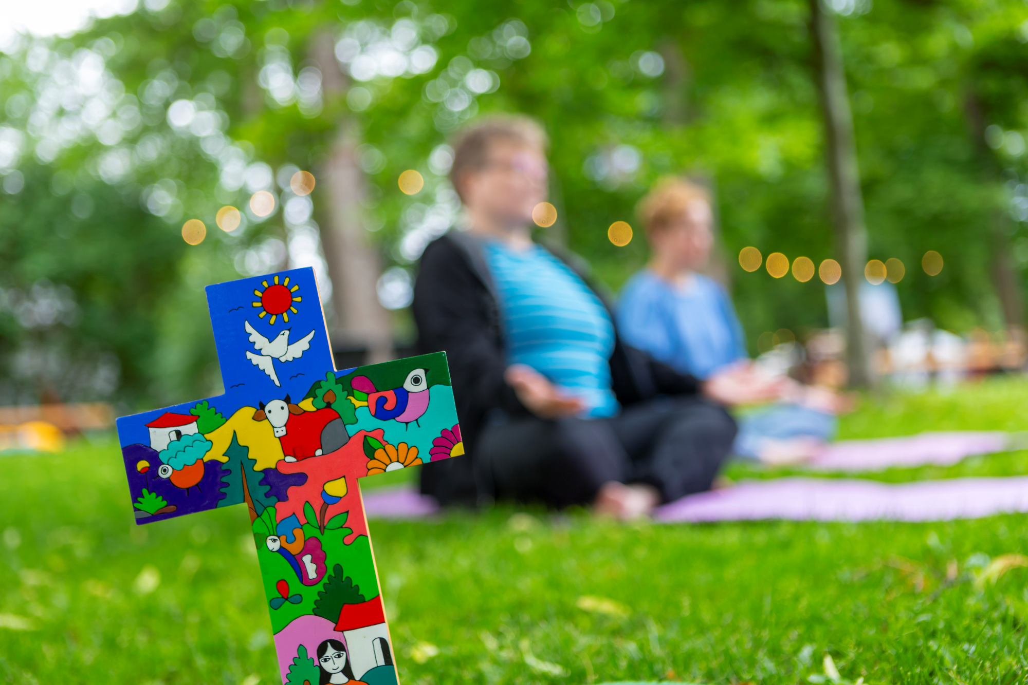 etualalla risti ja taka-alalla kaksi nurmikolla istujaa Tuomiokirkkopuistossa.