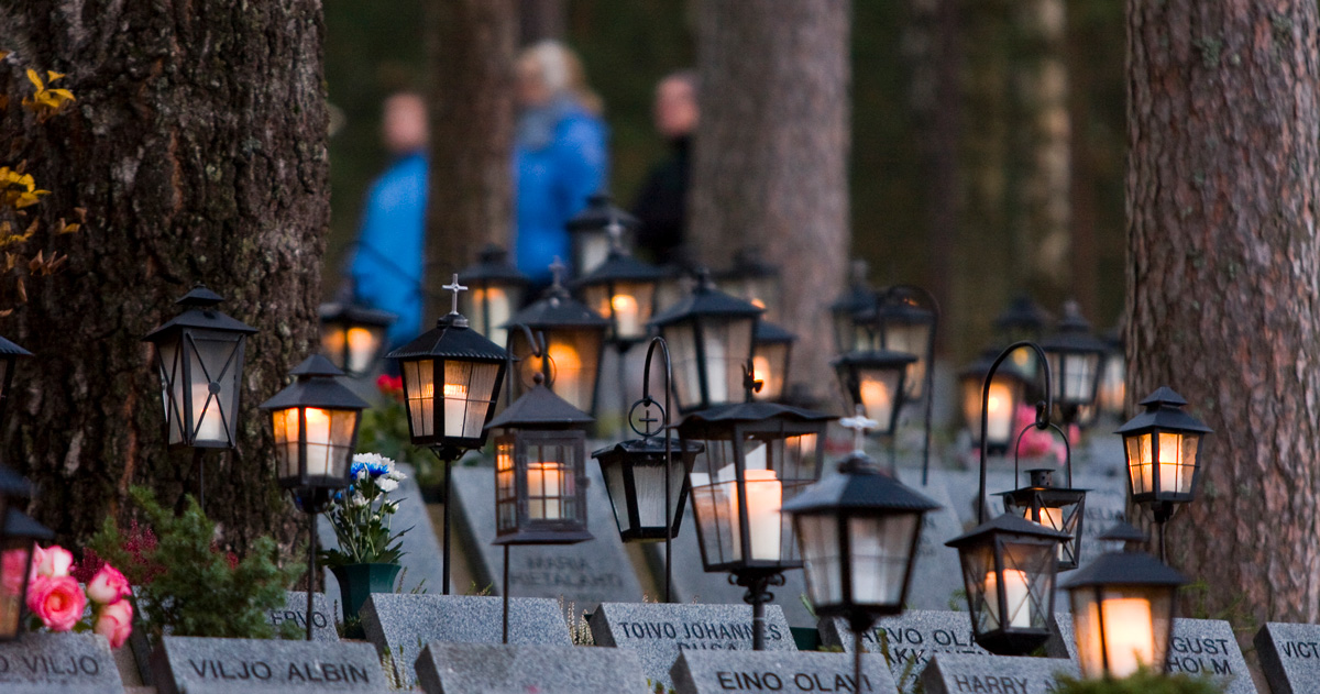 Kynttilälyhtyjä hautausmaalla, taustalla ihmishahmoja.