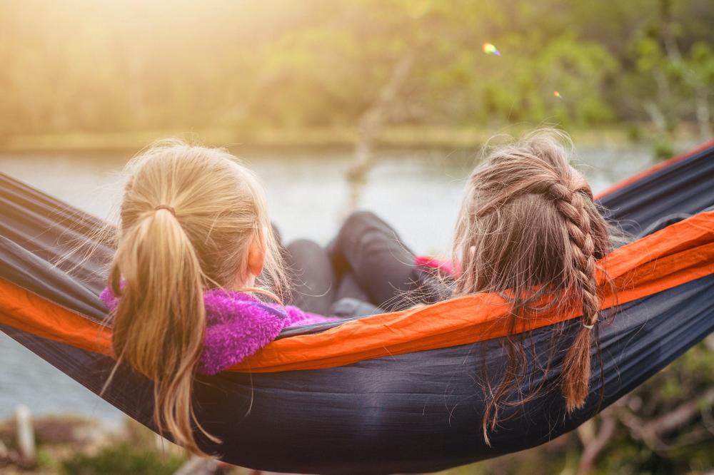Kaksi tyttöä makaavat vierekkäin riippukeinussa ja katsovat meren yli metsään. Kuvituskuva.