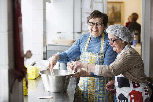 Kaksi hymyilevää naista leipoo keittiössä. Kuvituskuva.
