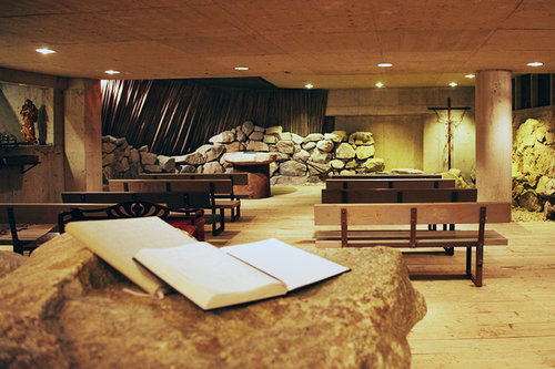 Sisäkuva kappelista, etualalla vanhan kiven päällä kirjoja, takana penkit
