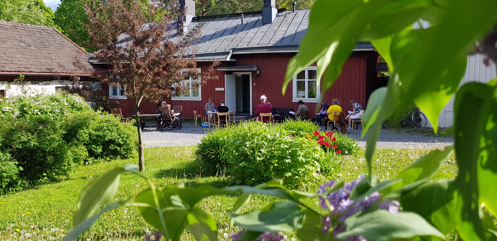 Yksinasuvien Kesäpiknik Nummella Nummen seurakuntakodin pihapiiri kesäisessä asussa. Ihmisiä istuskelemassa yhdessä.