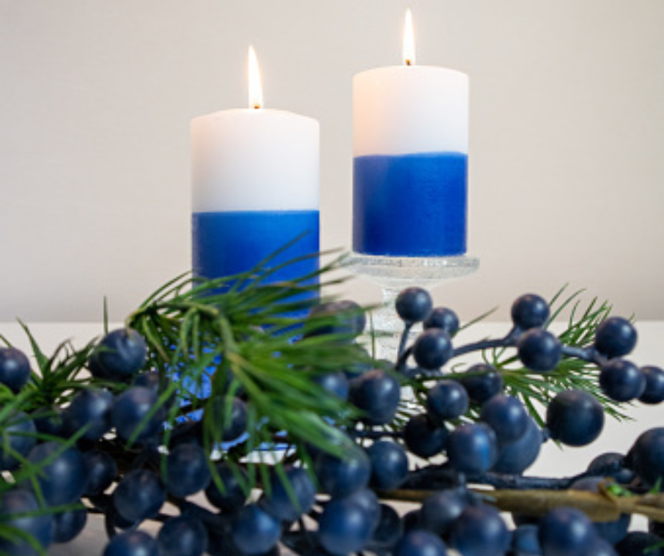 Kaksi sinivalkoista kynttilää joiden juurella mustikan oksa.