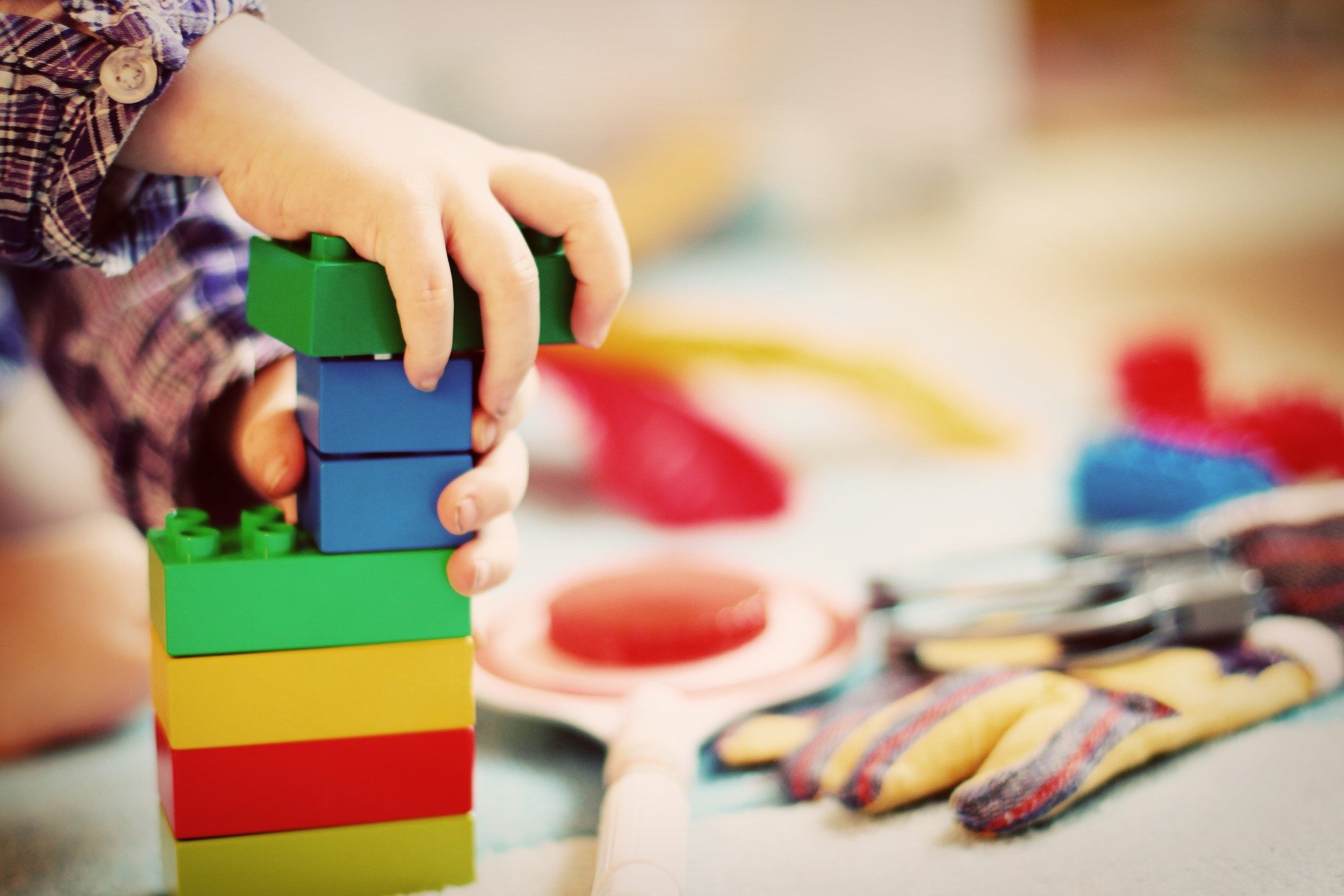 Kuvassa lapsen käsi, Lego-palikoita ja leluja.