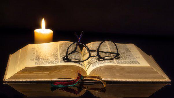 Raamattu jonka päällä silmälasit ja vieressä kynttilä.