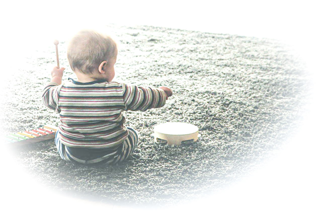 Vauva istuu lattialla matonpäällä, kädessä lyömäpuikot ja lattialla vieressä xylofoni ja tampuriini.