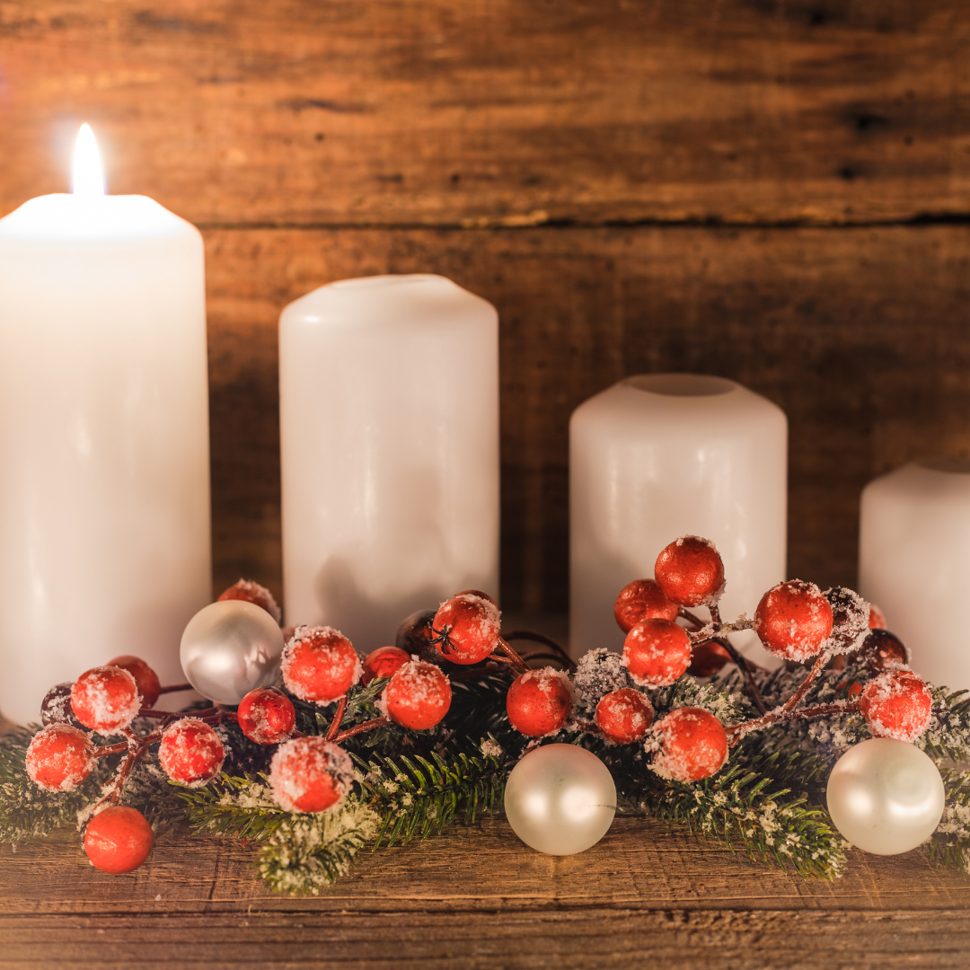 Neljä valkoista adventtikynttilää, joista yksi sytytetty. Edessä havuja, punaisia palloja ja kaksi valkoista joulupalloja koristeena.