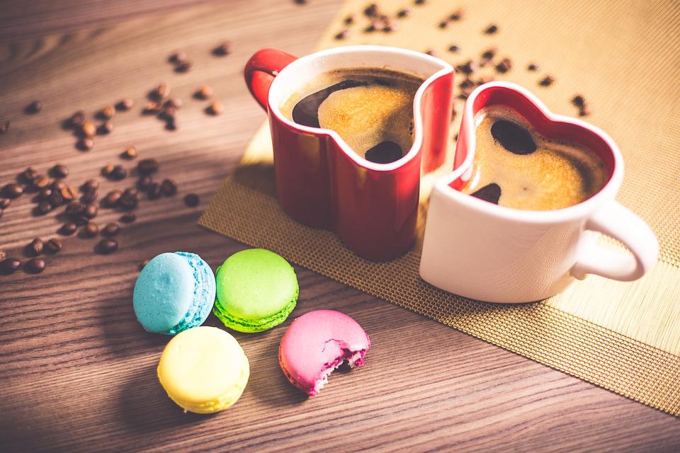 Puupöydällä kaksi sydämenmuotoista kahvikuppia ja macaron-leivoksia.