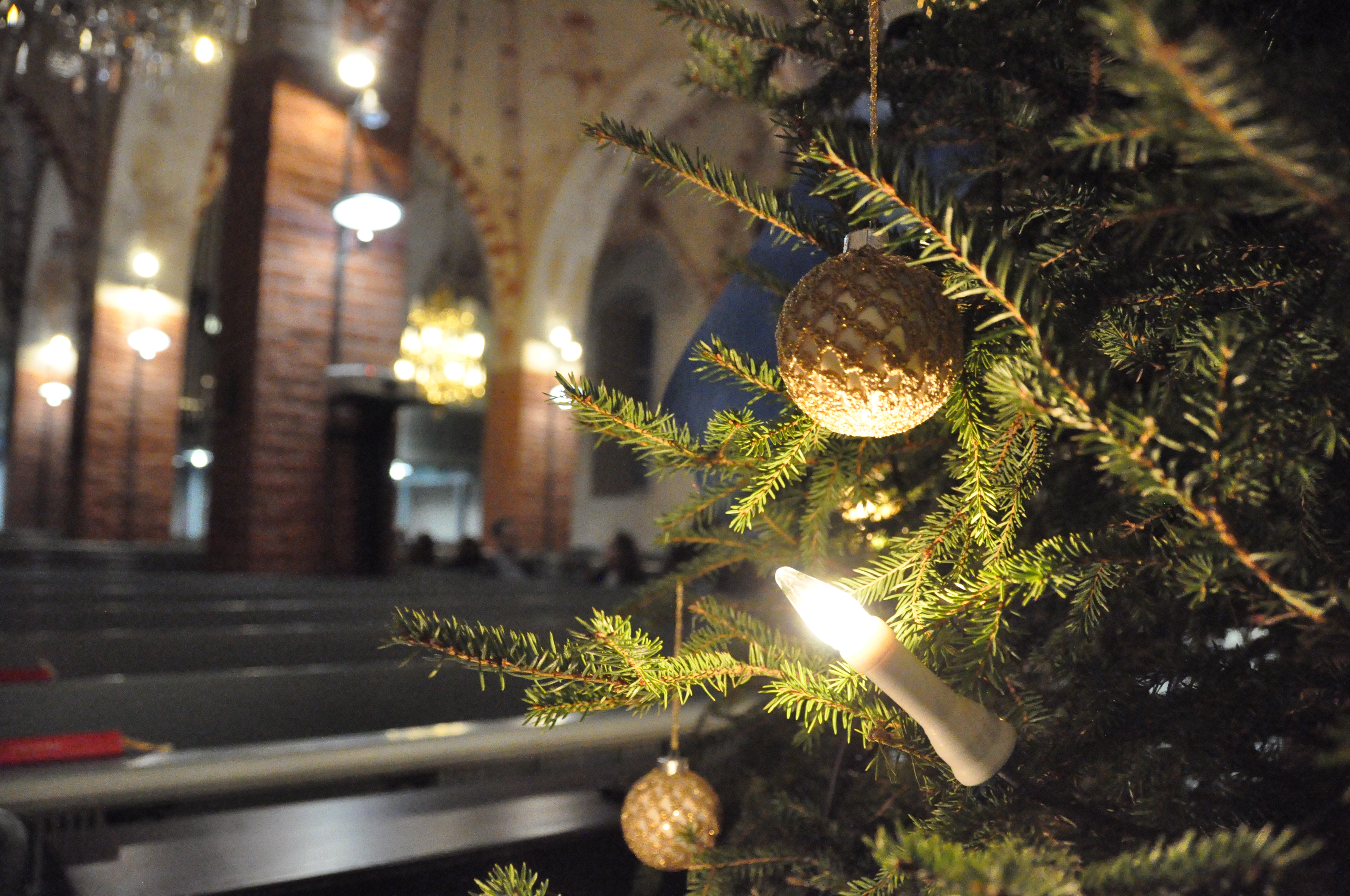 Joulukuusen oksilla palloja ja kynttilöitä, taustalla kirkon holvikaaria.