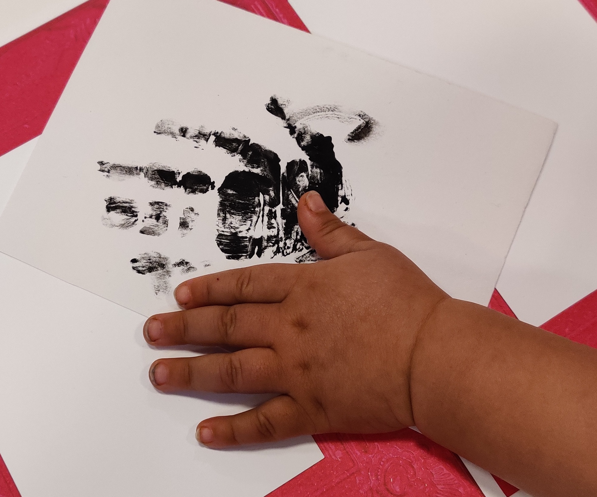 lapsen käsi pöydällä, jossa on paperilla maalattu käsi