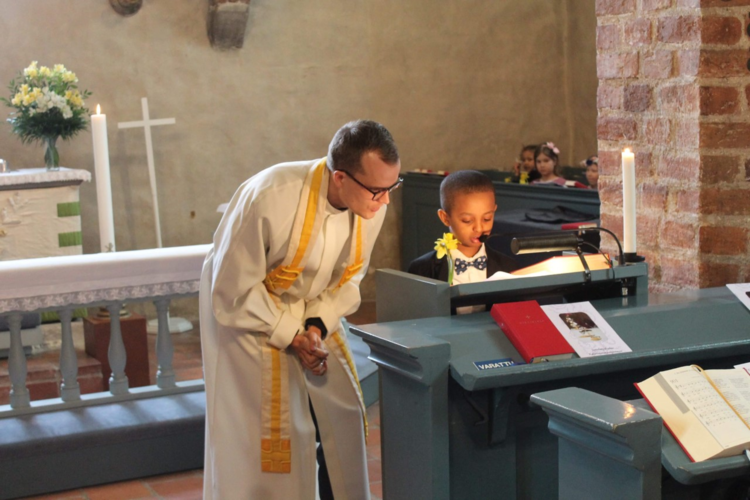 Kuvassa pappi ja pieni lapsi lukevat yhdessä esirukousta.