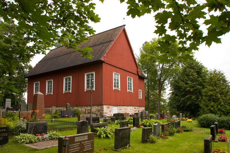 Punainen, harjakattoinen puukirkko, jonka edustalla hautausmaa.