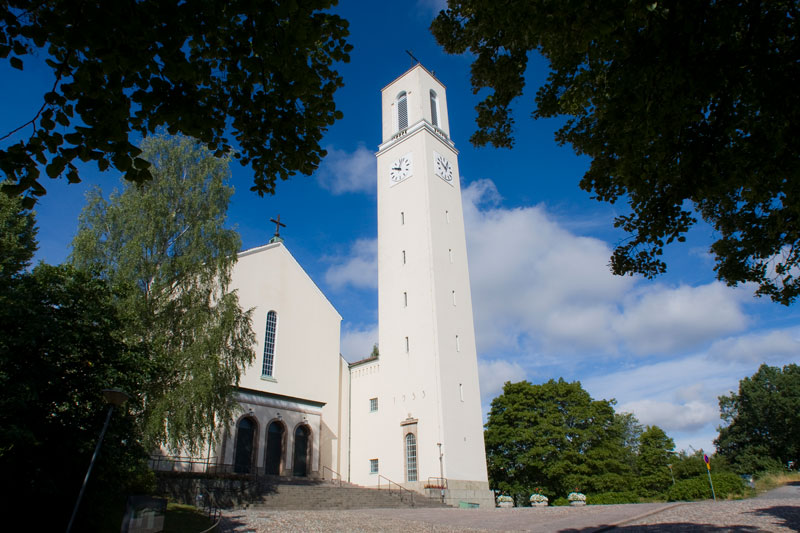 Valkoinen kirkko ja korkea kellotapuli kesäisessä maisemassa.