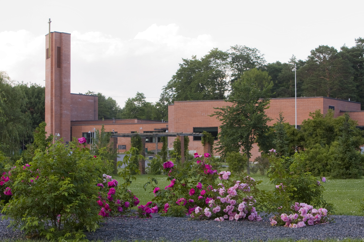 Punatiilinen kirkkorakennus, jonka edustalla kukkivia ruusupensaita.