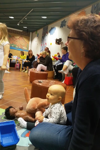 Perhetyöntekijä Jaana Heinonen leikkii pienen lapsen kanssa. Taustalla lapsia vanhempineen.