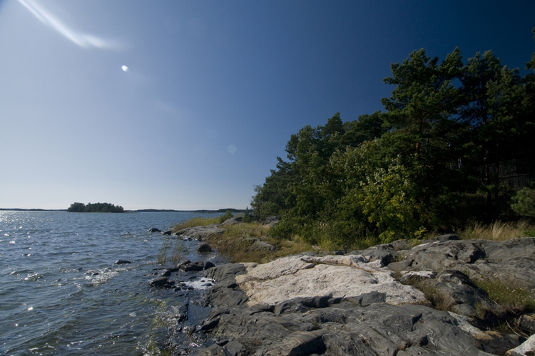 Merenranta, kallioita ja puita aurinkoisessa kesäsäässä.