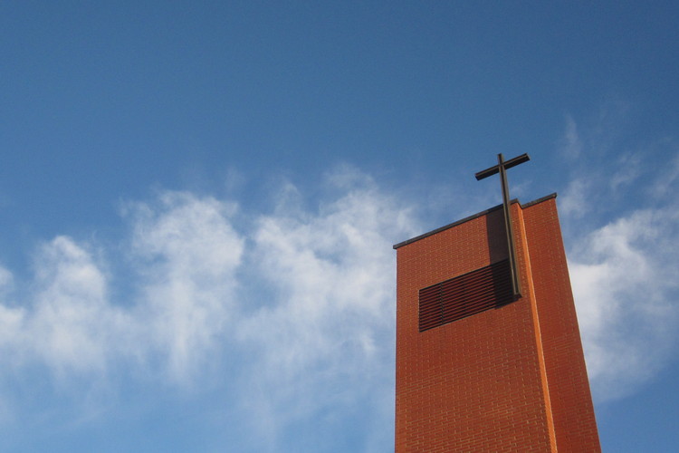 Kellotapulin harja risteineen sinistä taivasta ja pilvenhahtuvia vasten.