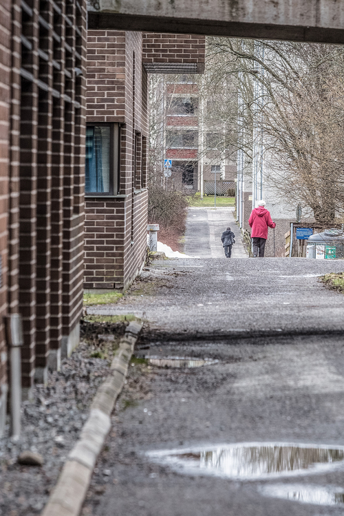 vanha nainen kävelee kaukana taustalla katua pitkin