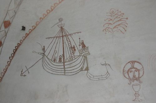 Valkeaksi kalkitulla seinällä punavärillä piirretty laiva sekä Kristuksen kasvot