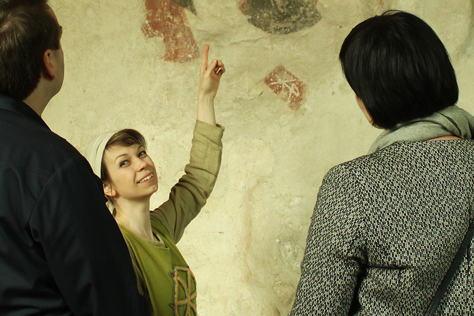 Iloinen keskiaikapukuun pukeutunut nainen osoittaa kirkon seinää