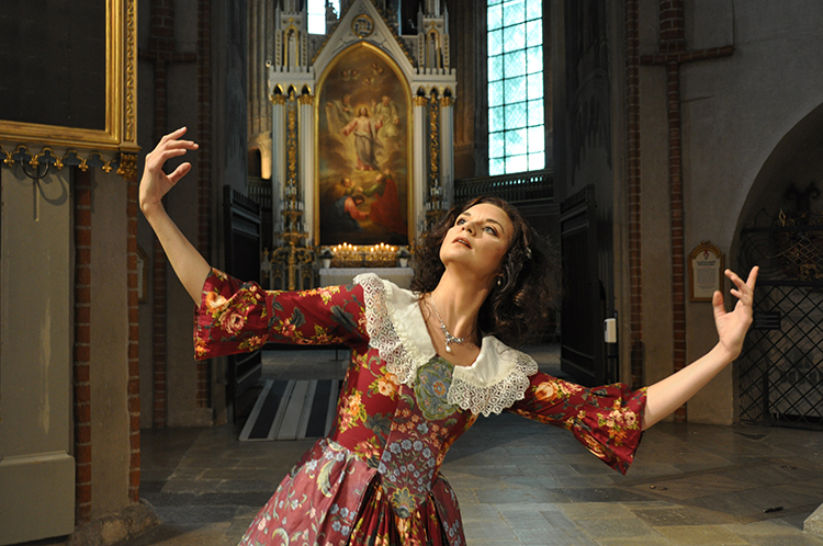 1600-luvun tyylisin vaatteisiin pukeutunut nainen tanssii Turun tuomiokiron alttari takanaan.