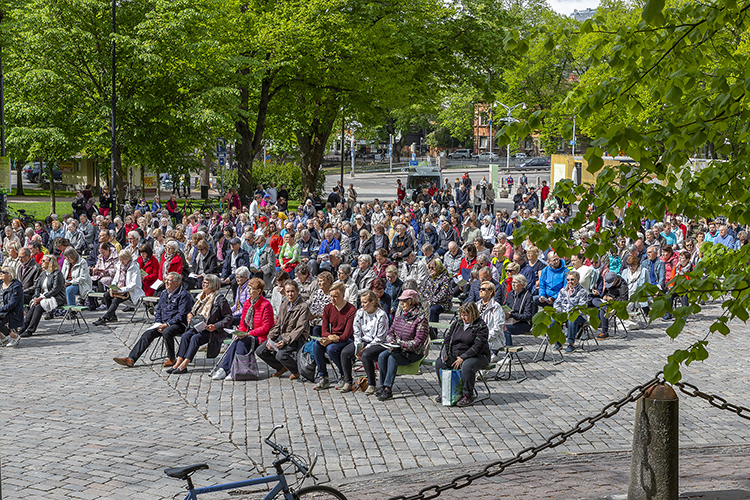 Suuri määrä ihmisiä istuu penkeillä Turun tuomiokirkkotorilla kuuntelemassa jumalanpalvelusta.