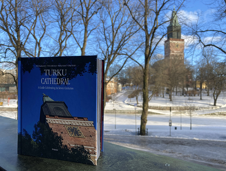 Turku Cathedral -opaskirja parvekkeen kaiteella pystyssä. Taustalla on sumeana talvinen Turun Tuomiokirkko.