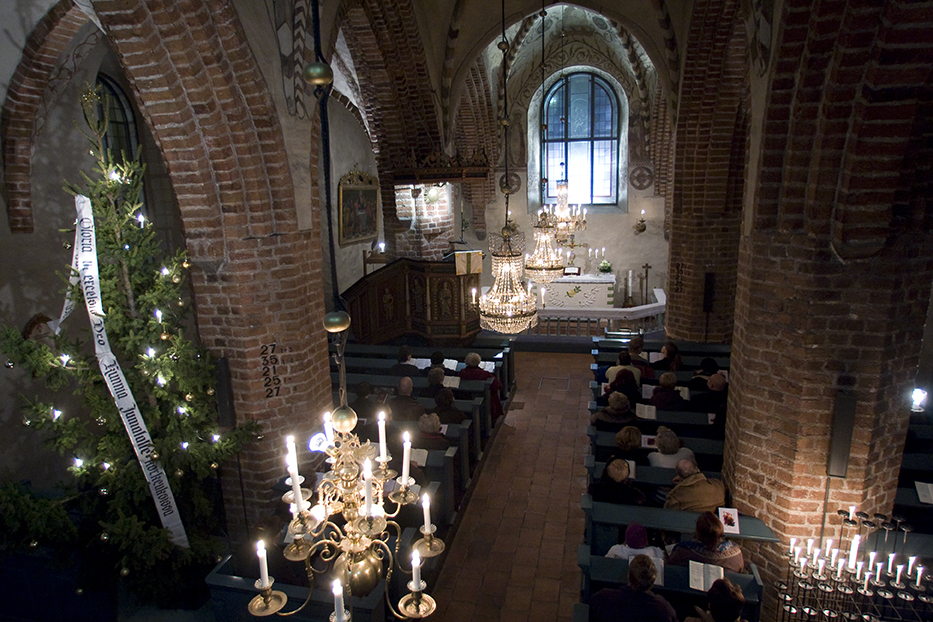 Kirkkosali jossa valaistu joulukuusi ja seurakuntalaisia istumassa.