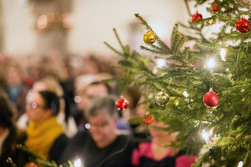 Koristeltu kuusi ja kirkonpenkissä istuvia ihmisiä.