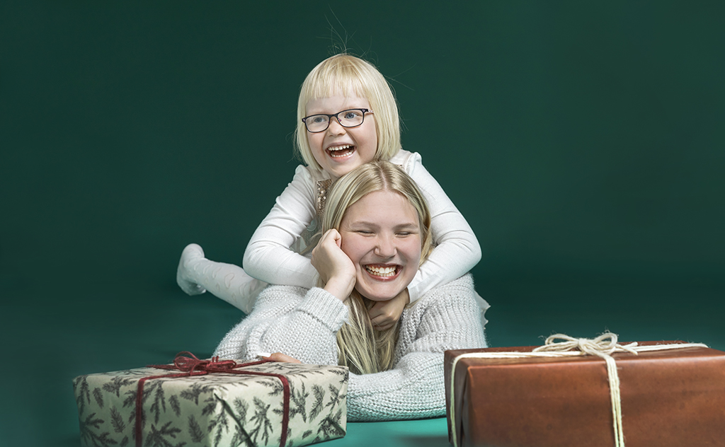 Teini-ikäinen ja leikki-ikäinen tyttö makaavat lattialla, kuvan etualalla on joulupaketteja.