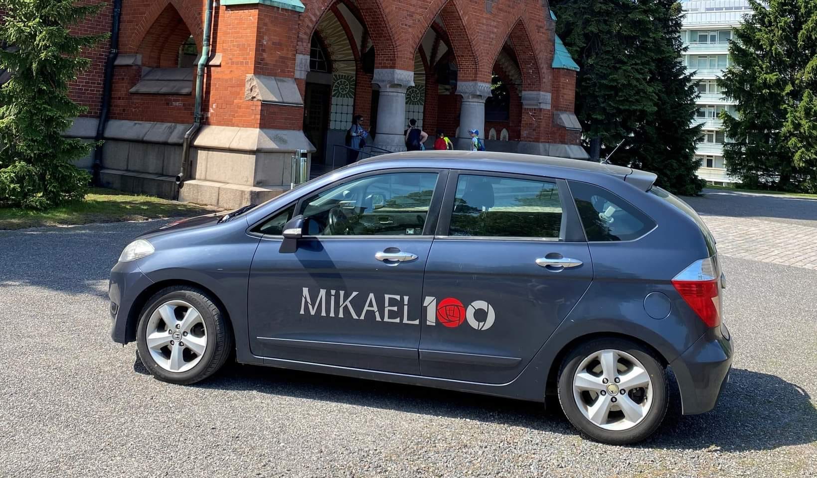 Mikael100-tarroilla koristeltu auto Mikaelinkirkon edustalla.