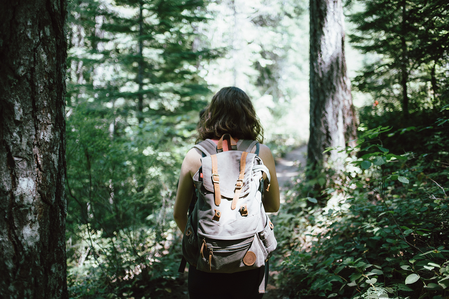 Nainen kävelee metsässä reppu selässä selvä kameraan päin.