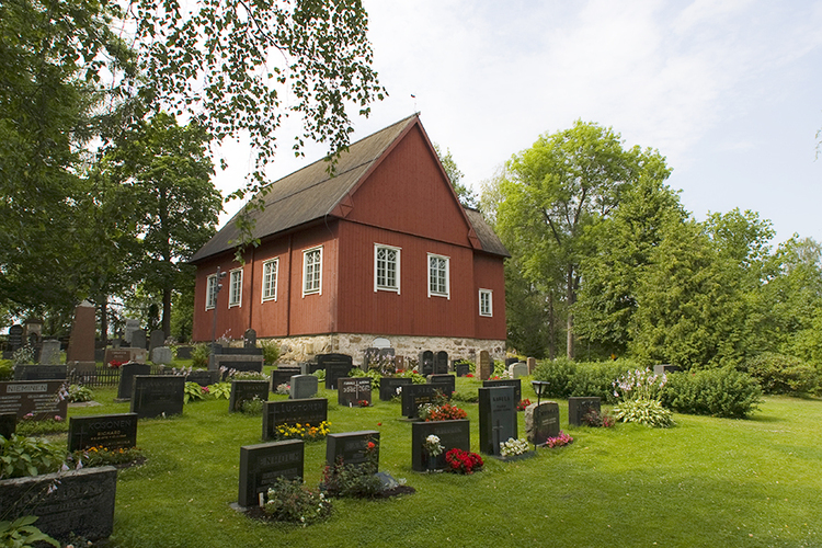 Hautakivien ja nurmikon ympäröimä punainen vanha puurakennus.