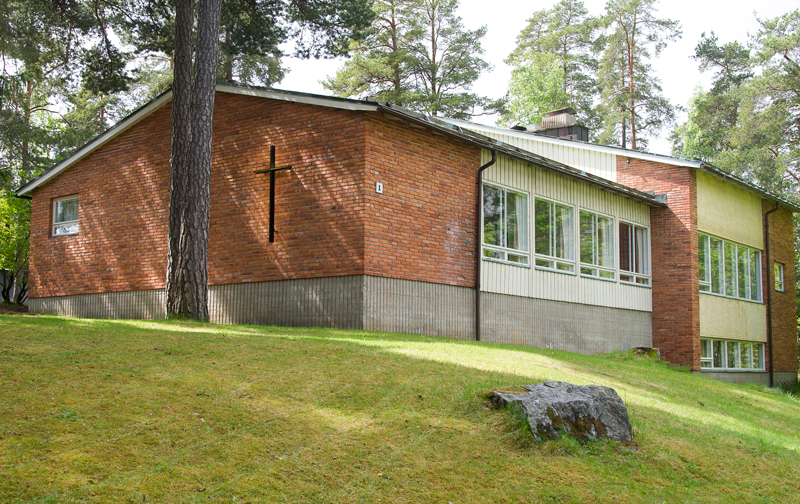 Ulkokuva Littoisten seurakuntatalosta. Punatiilinen, matala rakennus mäntyjen keskellä.