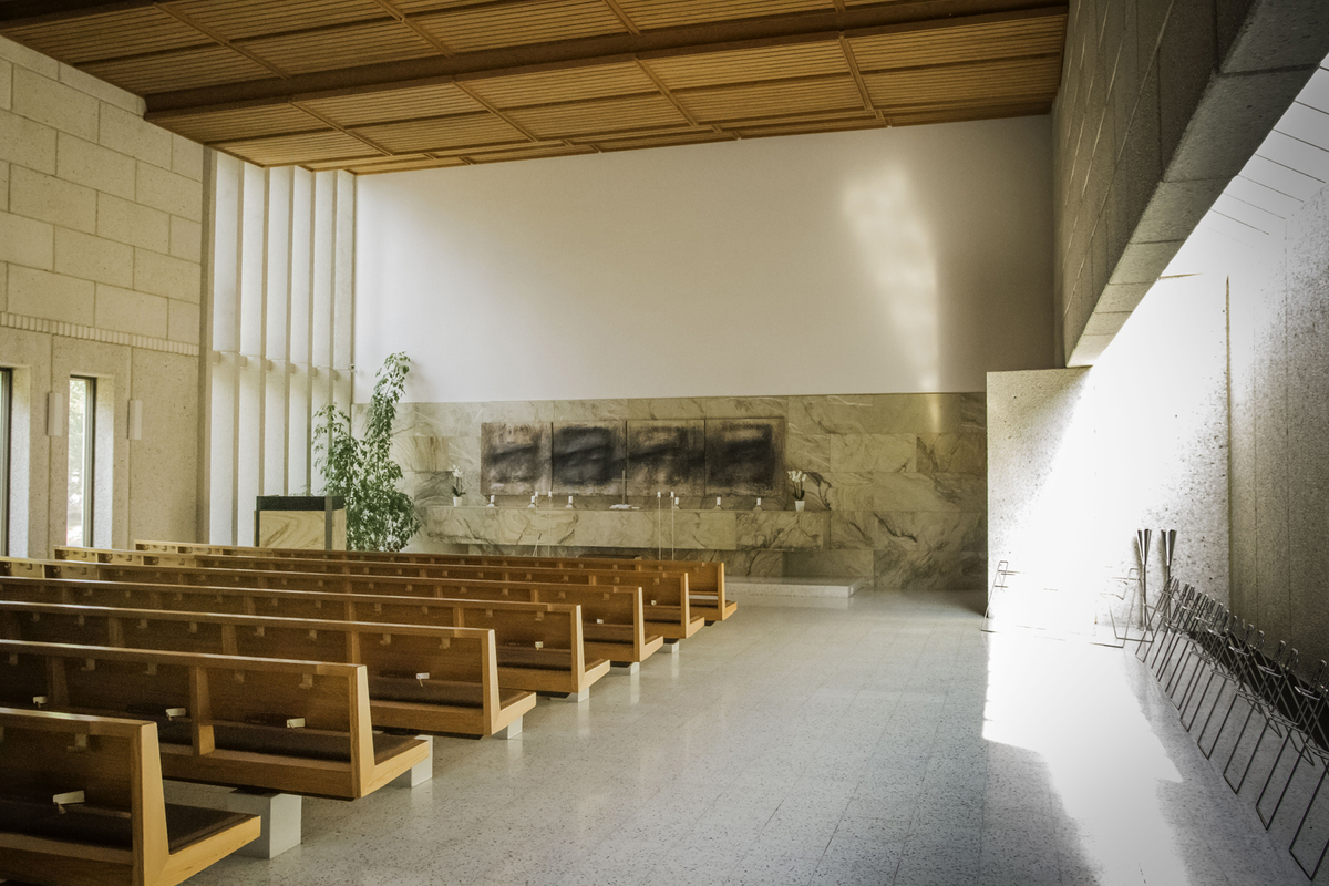 Sisäkuva valoisasta kappelista, jossa puiset penkkirivit ja niiden edessä alttari.
