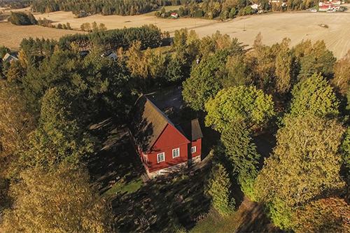 Red wooden church from bird eye view. Around the church lots of trees and field.