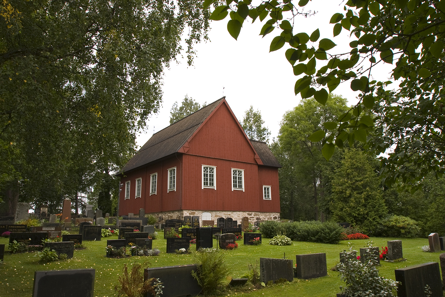 Red wooden church surrounded by trees. In front of the church there's a graveyard. Photo: Timo Jakonen.