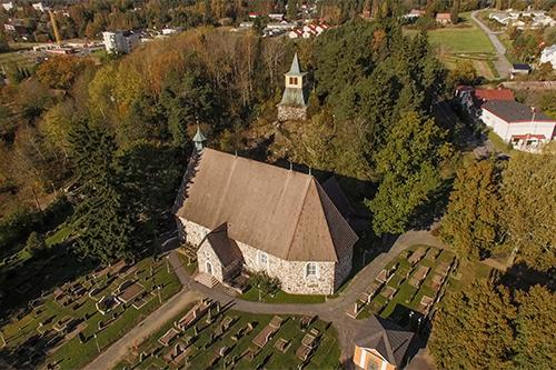 Stone church from bird eye view. Lots of trees and a graveyard around the building.